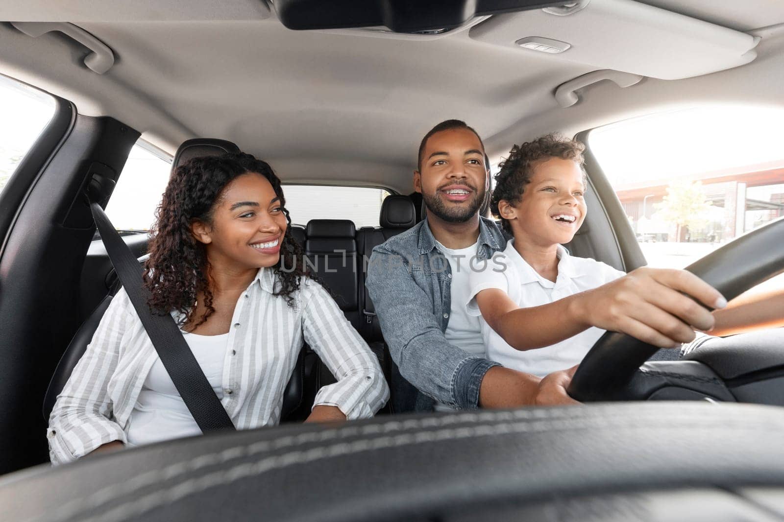 African American Father Teaching His Son To Drive Driving The Car Together. Happy Family Riding New Automobile In City, Having Fun Traveling By Auto. Vehicle Transportation