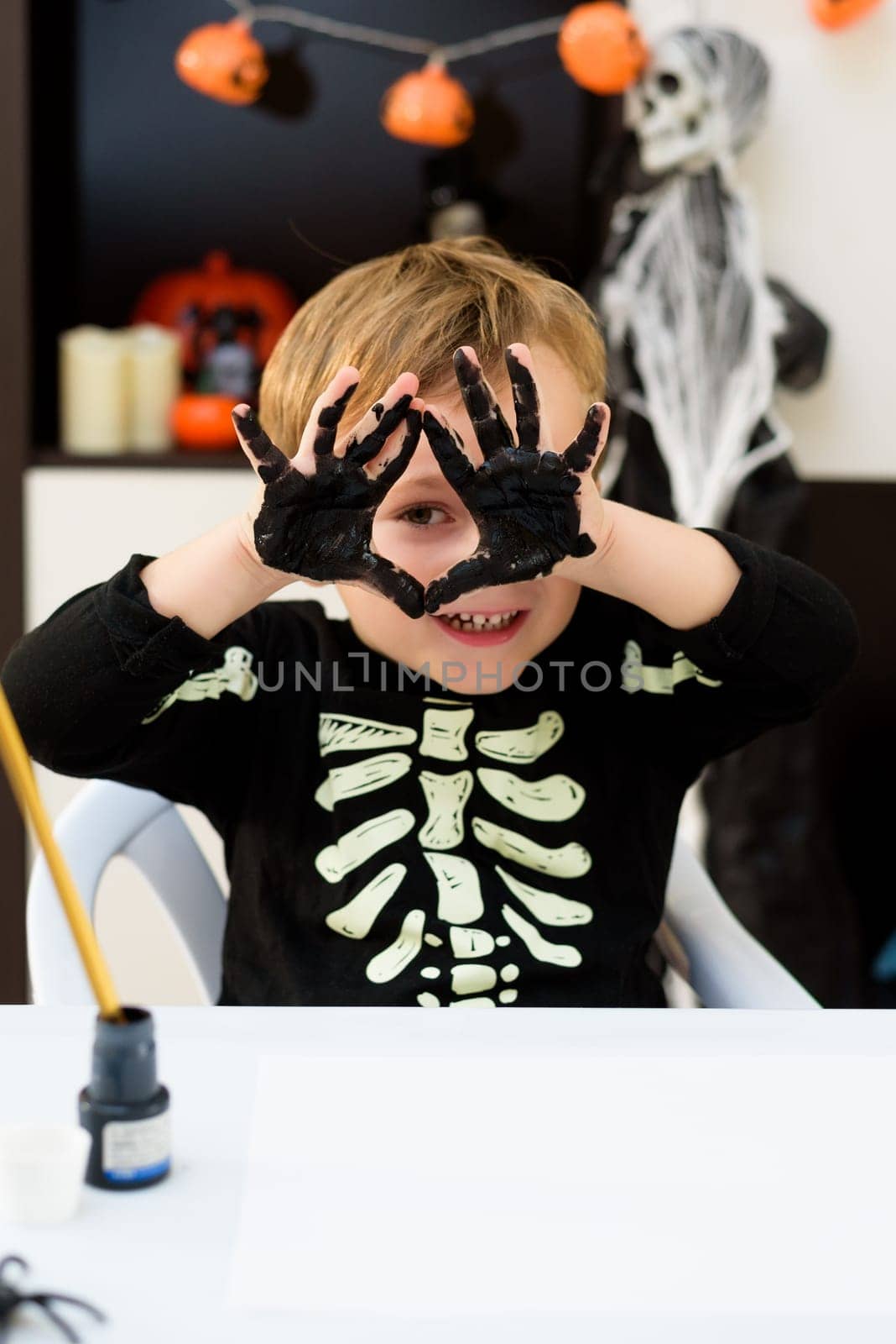 A child dressed as a skeleton shows spider and ghost crafts. Halloween party by jcdiazhidalgo