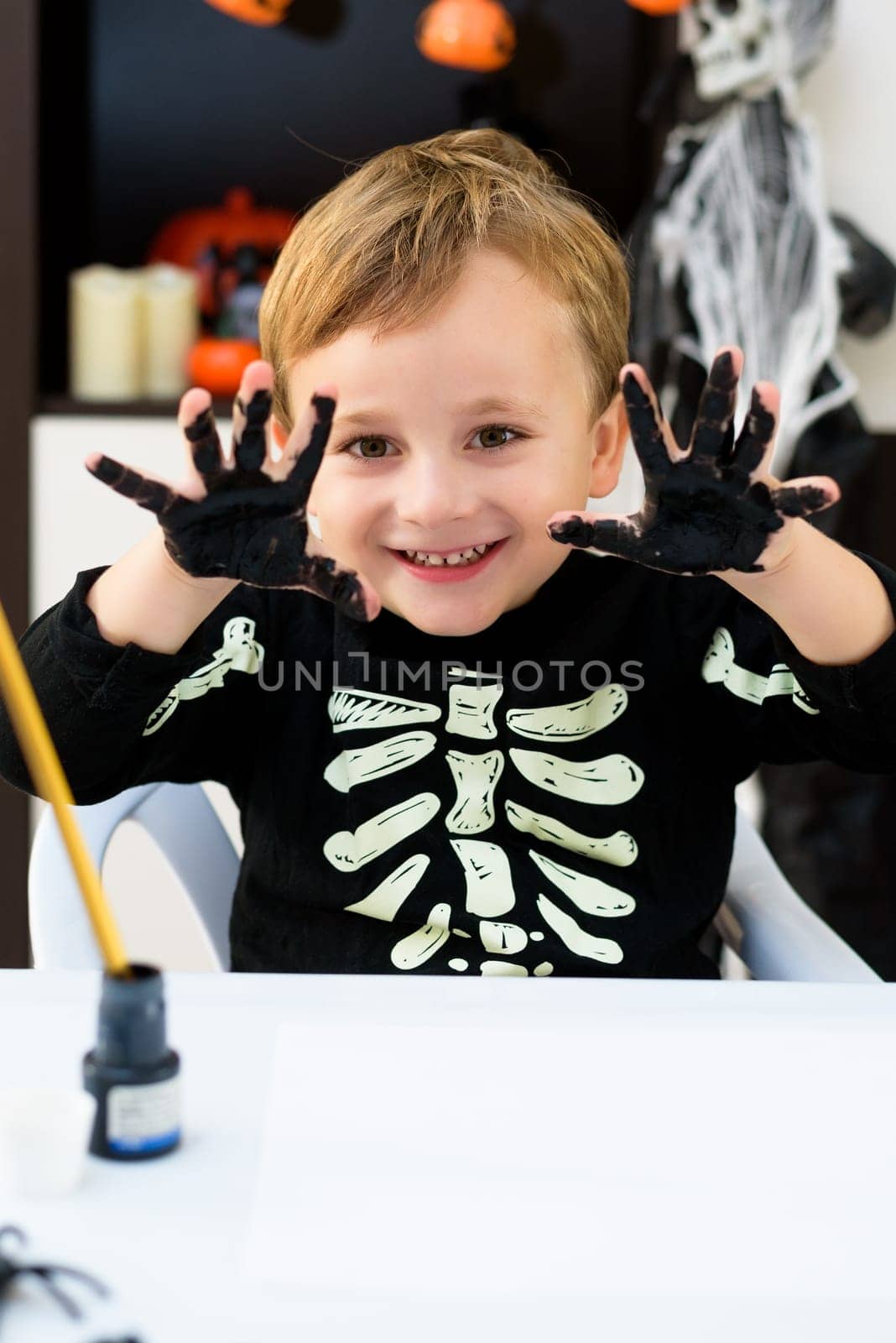 A child dressed as a skeleton shows spider and ghost crafts. Halloween party.