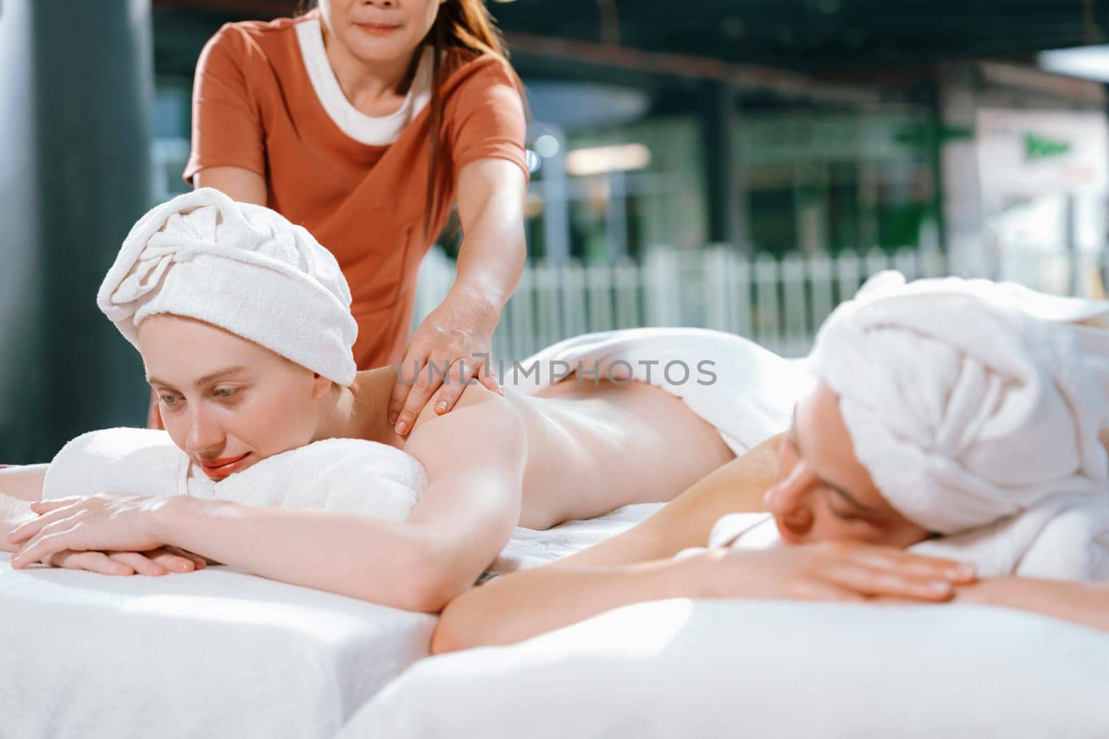 Couple of beautiful young woman lie on white spa bed during having back massage. Attractive caucasian woman having back massage at traditional spa room. Relaxing and healthy concept Tranquility.