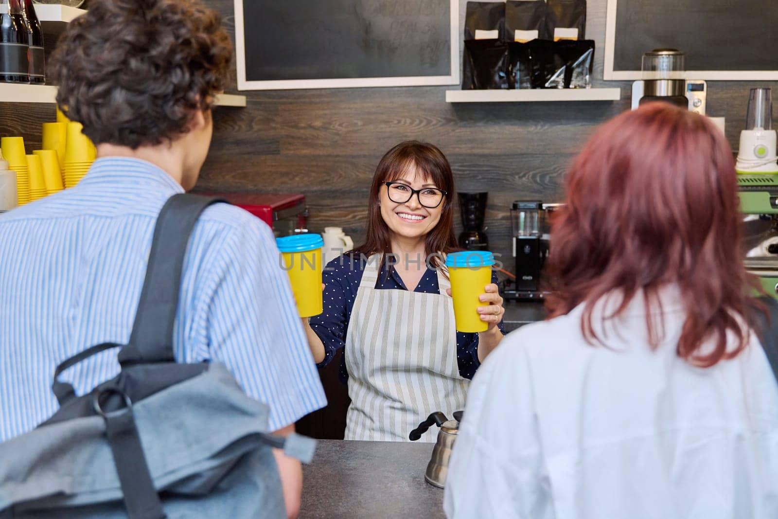 Female coffee shop worker serving customers giving paper cups of takeaway coffee by VH-studio