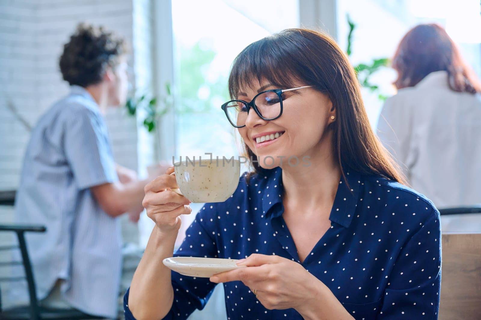 Relaxed happy middle aged woman enjoying fragrant fresh tasty cup of coffee while sitting in coffee shop. Coffee culture, lifestyle, people concept