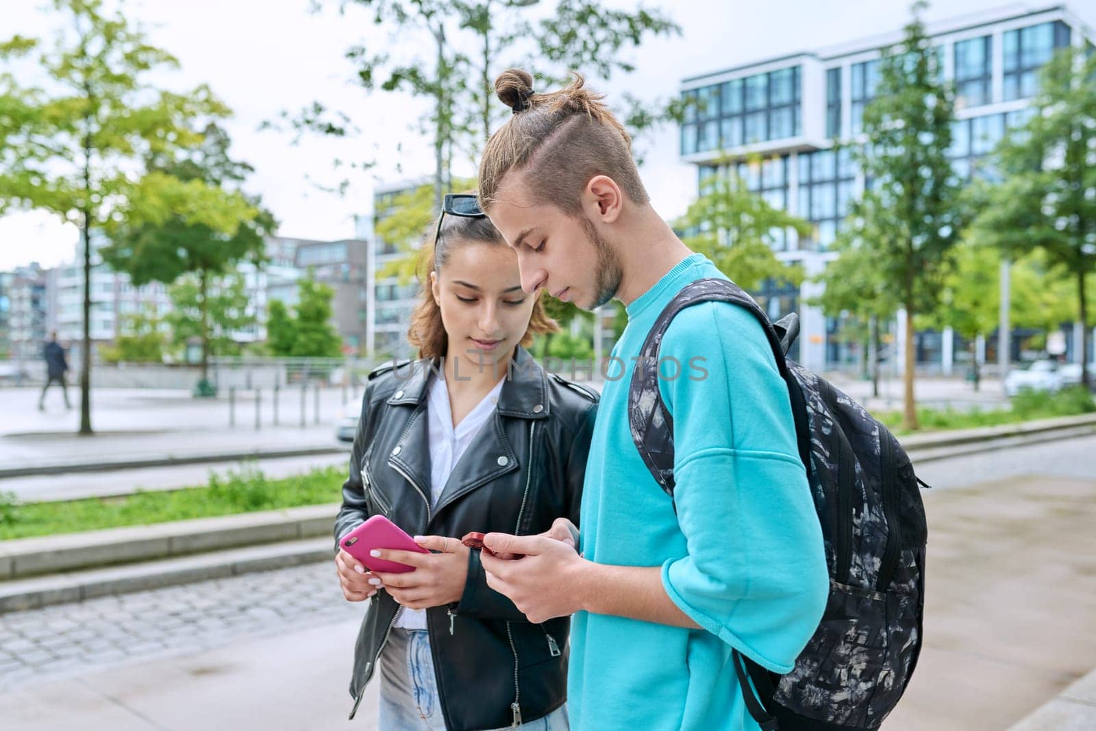 Teenage friends guy and girl standing together using smartphones by VH-studio