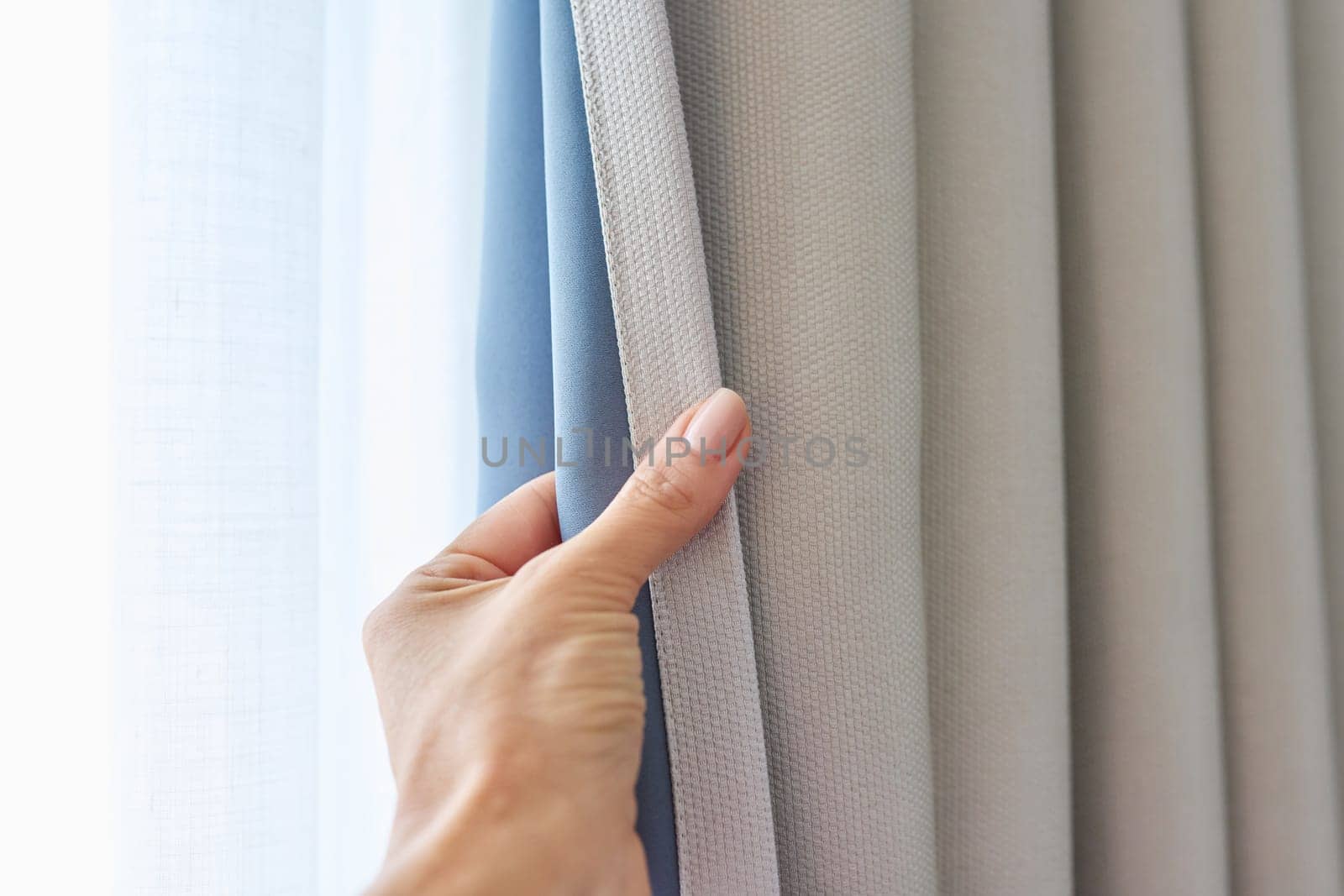 Woman's hand showing light gray curtain on blue opaque lining, fabric blackout by VH-studio