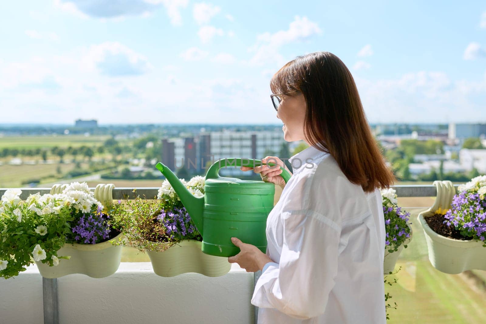 Woman watering potted plants from watering can on outdoor terrace at home. Green hobby, home gardening, eco trends