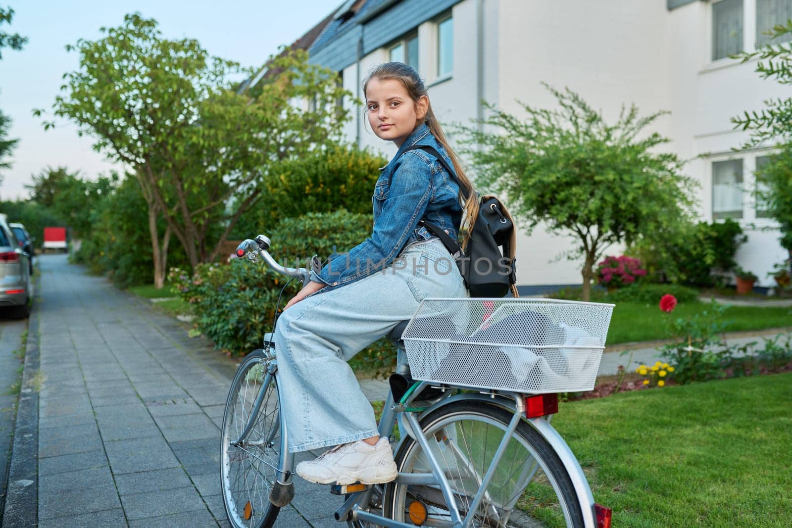 Back to school. Girl child 10, 11 years old with backpack on bicycle on street near house, posing looking at camera. Schoolgirl cycling to school, lifestyle, childhood concept