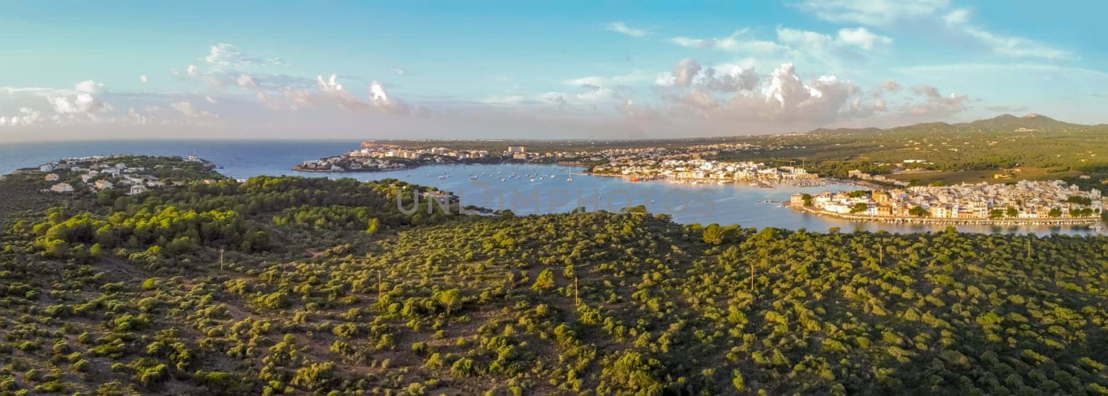 panoramic drone aerial view of the mediterranean sea at sunrise darsena, lagoon and fishing port, typical area of tourist interest, holiday destinations and hotel zone in portocolom,mallorca,balearic islands, lighthouse on the cliffs