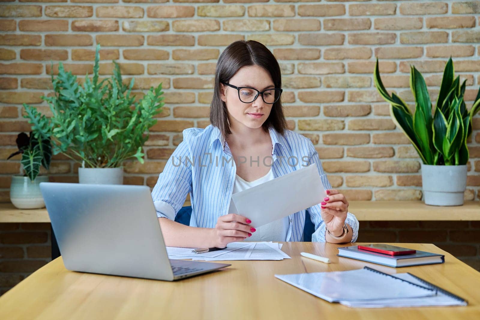 Young business woman with paper letter sitting at desk with computer in office. Business, bank chat payments, contracts, agreements, business people concept