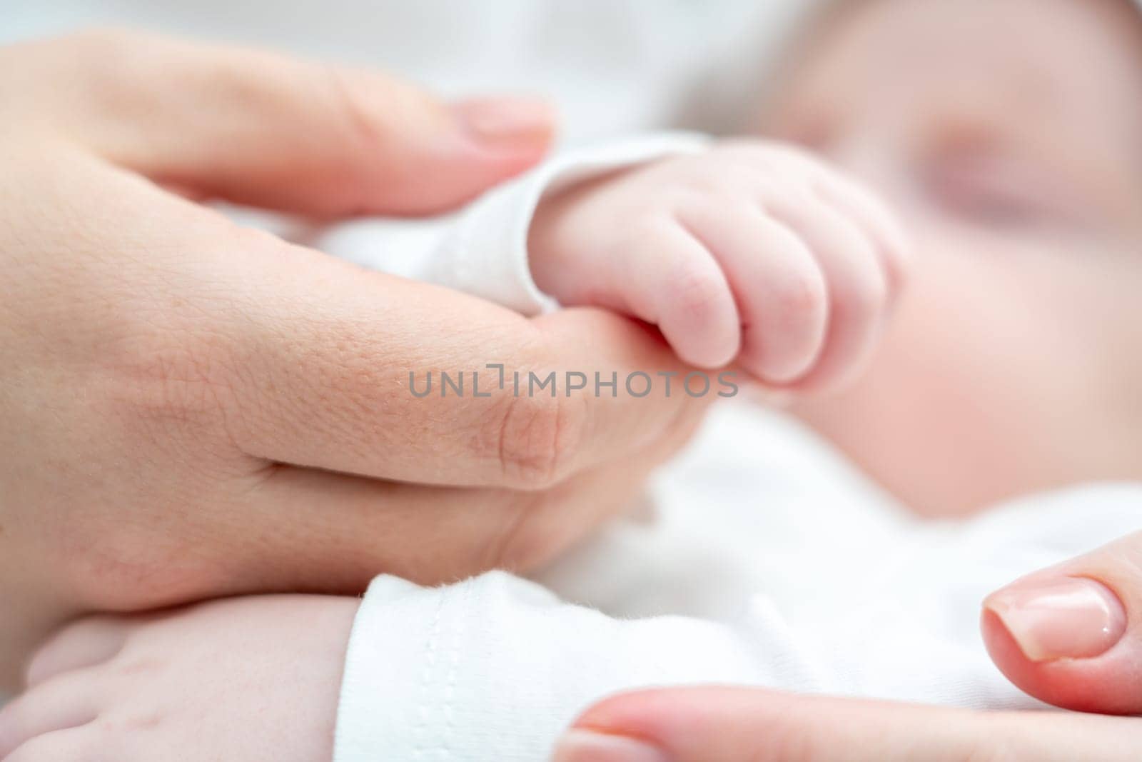 Close-up portrays a sleeping newborn baby softly gripping mother's finger, symbolizing trust and care