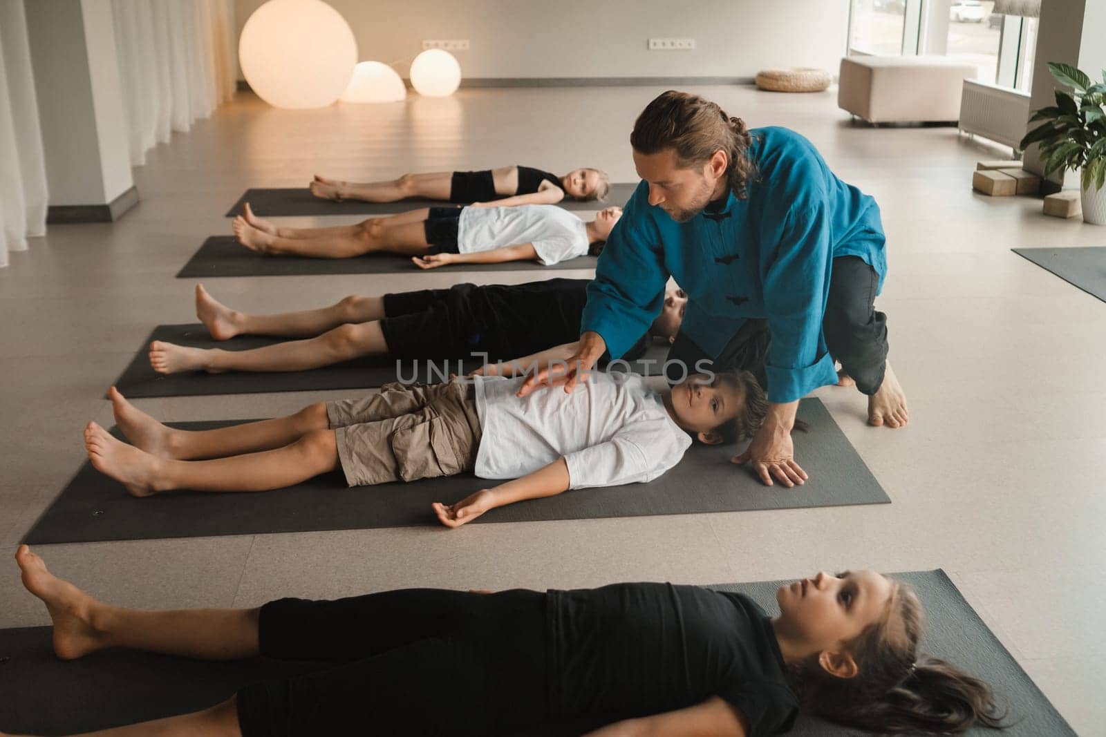 A yoga instructor trains children lying on mats in the fitness room. Children's yoga.