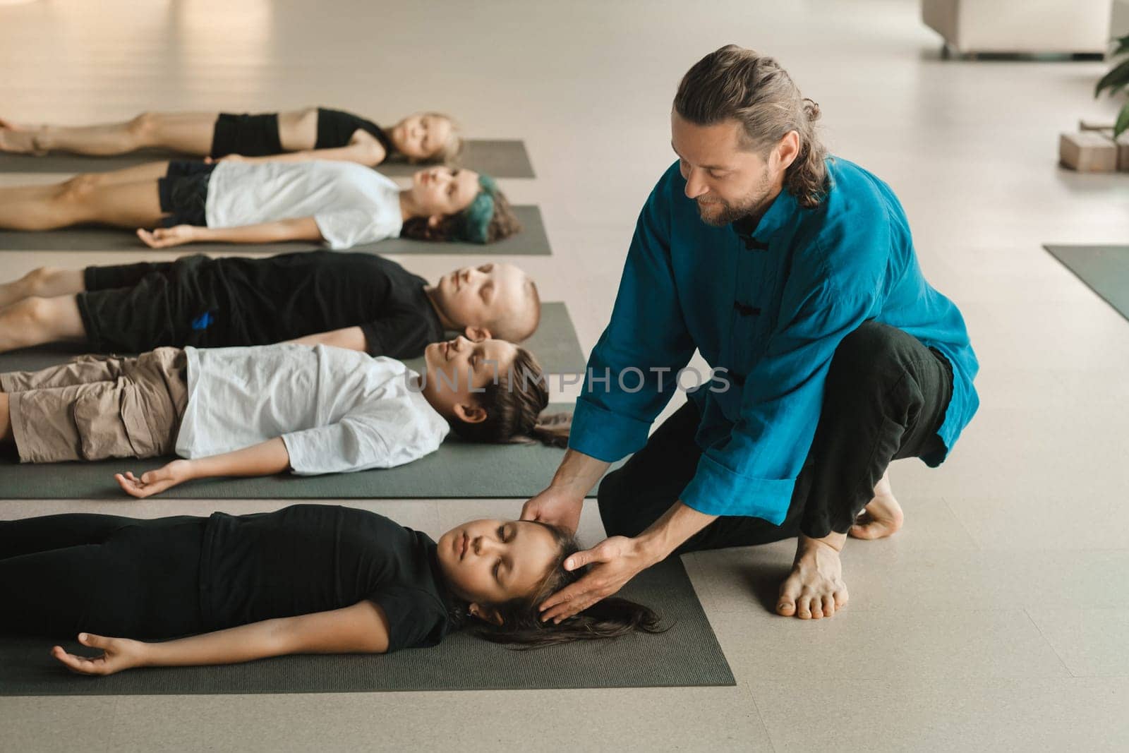 A yoga instructor trains children lying on mats in the fitness room. Children's yoga by Lobachad
