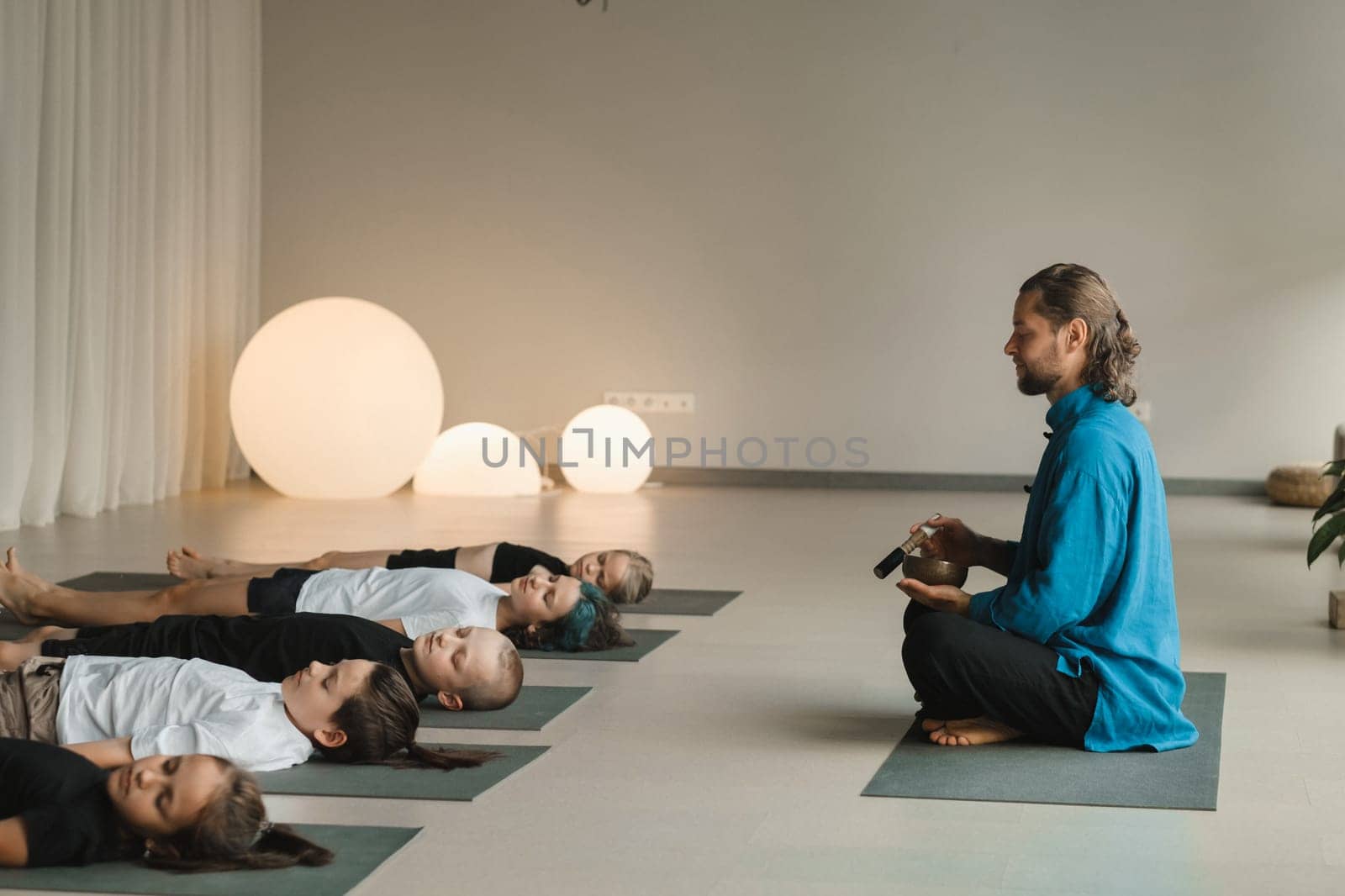 Children relax lying down to the sounds of a Tibetan bowl in the fitness room. Children's yoga.