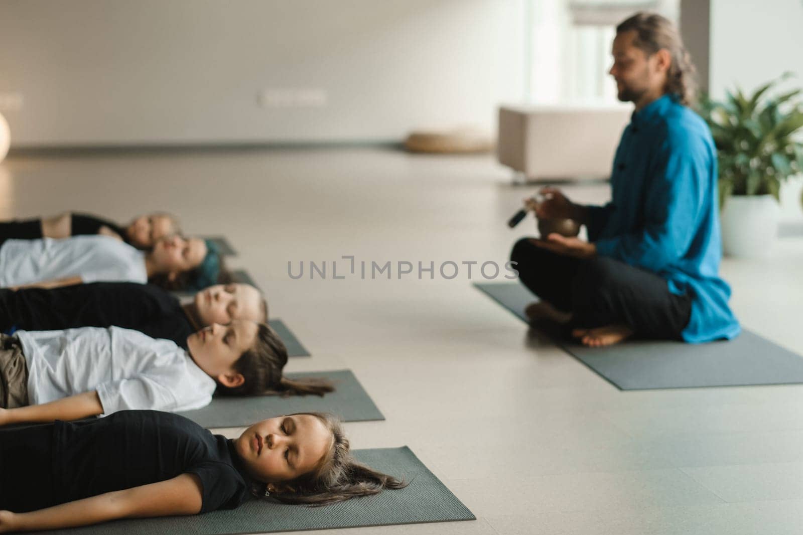 Children relax lying down to the sounds of a Tibetan bowl in the fitness room. Children's yoga.