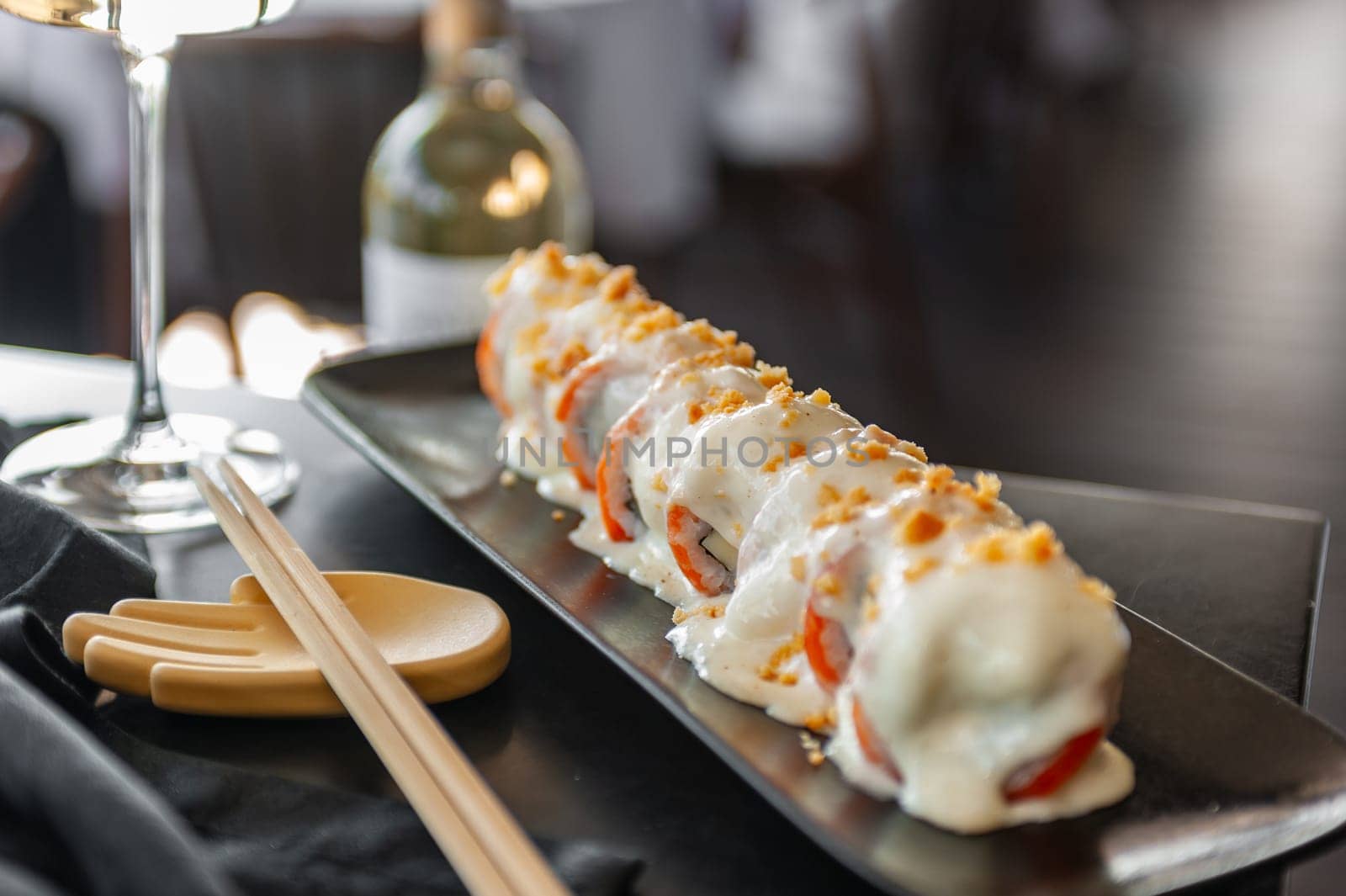 Sushi roll with salmon and vegetables in sauce on a black plate in a restaurant. High quality photo