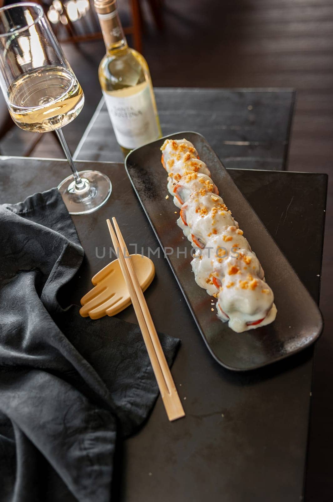 Sushi roll with salmon and vegetables in sauce on a black plate in a restaurant. High quality photo