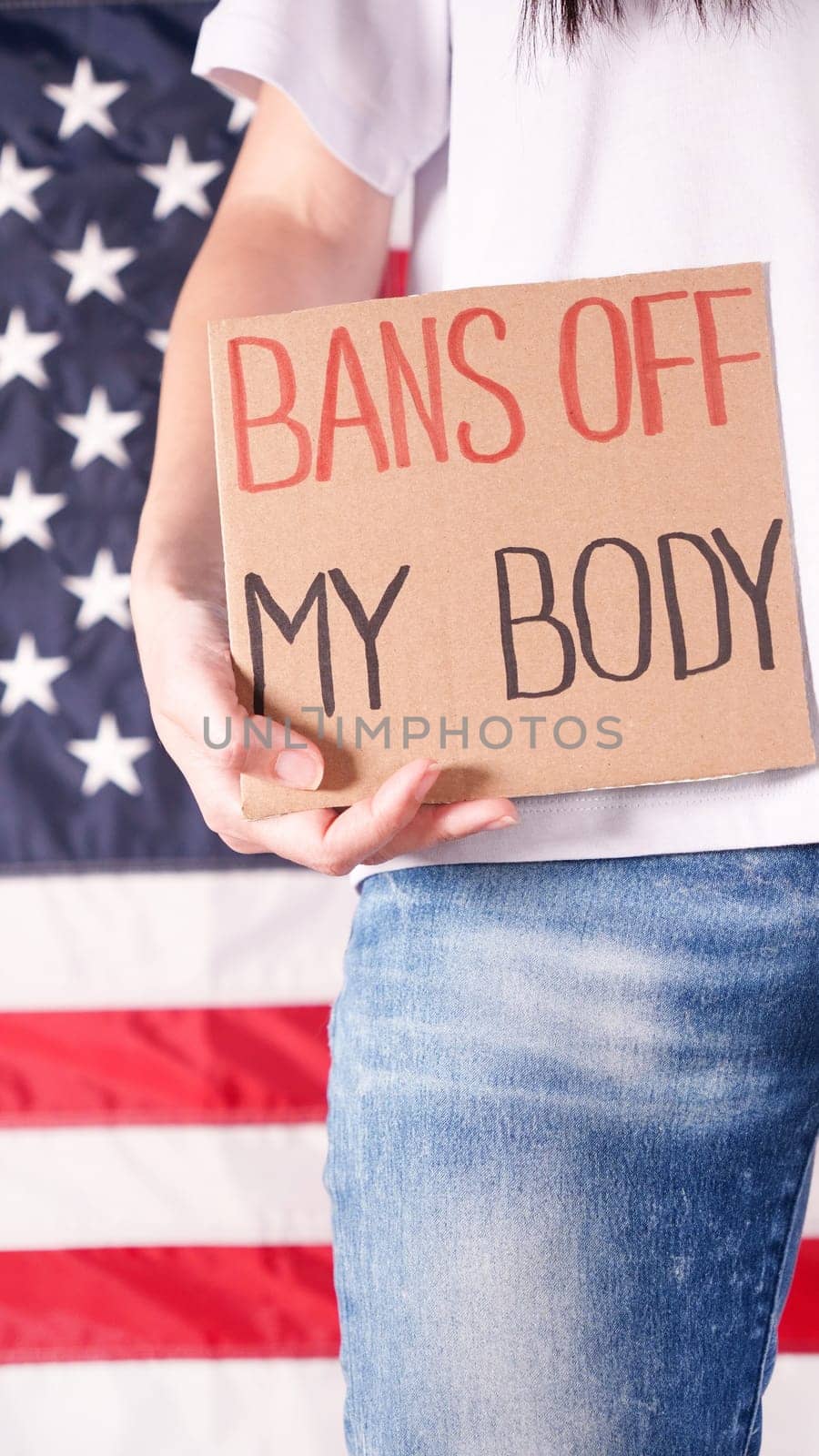 Woman holding a sign Bans Off My Body American flag on background. Protest against anti abortion law. Women's strike. Womens rights freedom