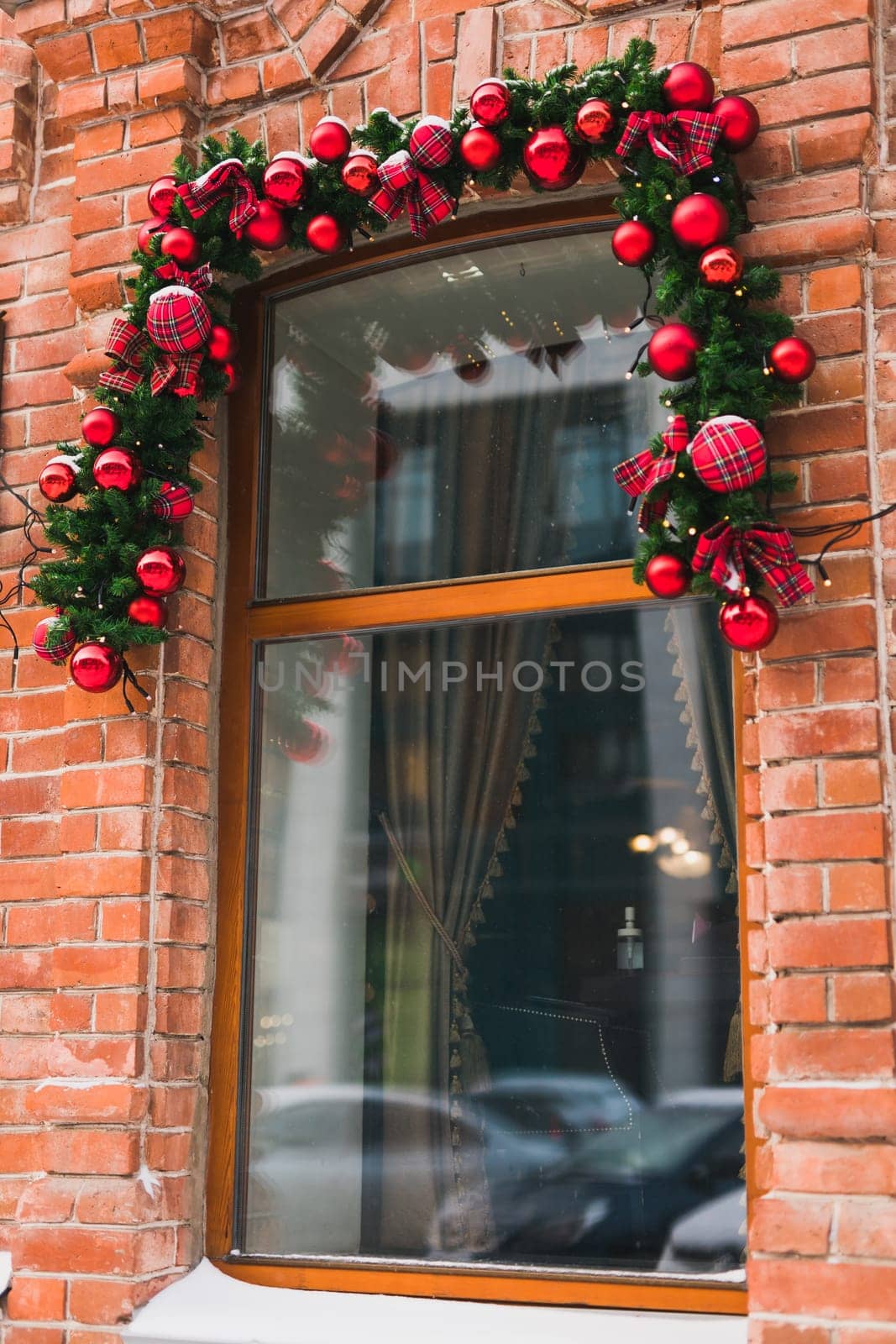 Stylish christmas fir branches with red baubles and sparkling garland on front of window at holiday market or restaurant in city street. Winter christmas street decor by Satura86