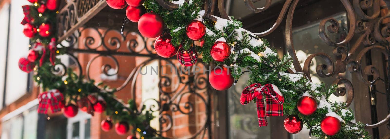 Banner stylish christmas fir branches with red baubles and sparkling garland on front of door at holiday market or restaurant in city street. Winter christmas street decor by Satura86