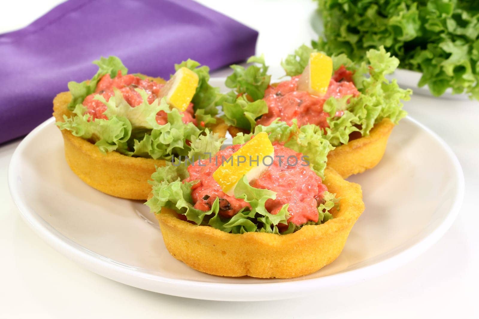 Corn tartlets with pollock salad against a white background