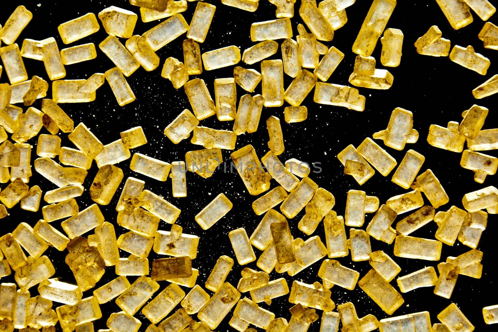 Macro of refined crystallised sugar with rectangular golden granules on a dark background