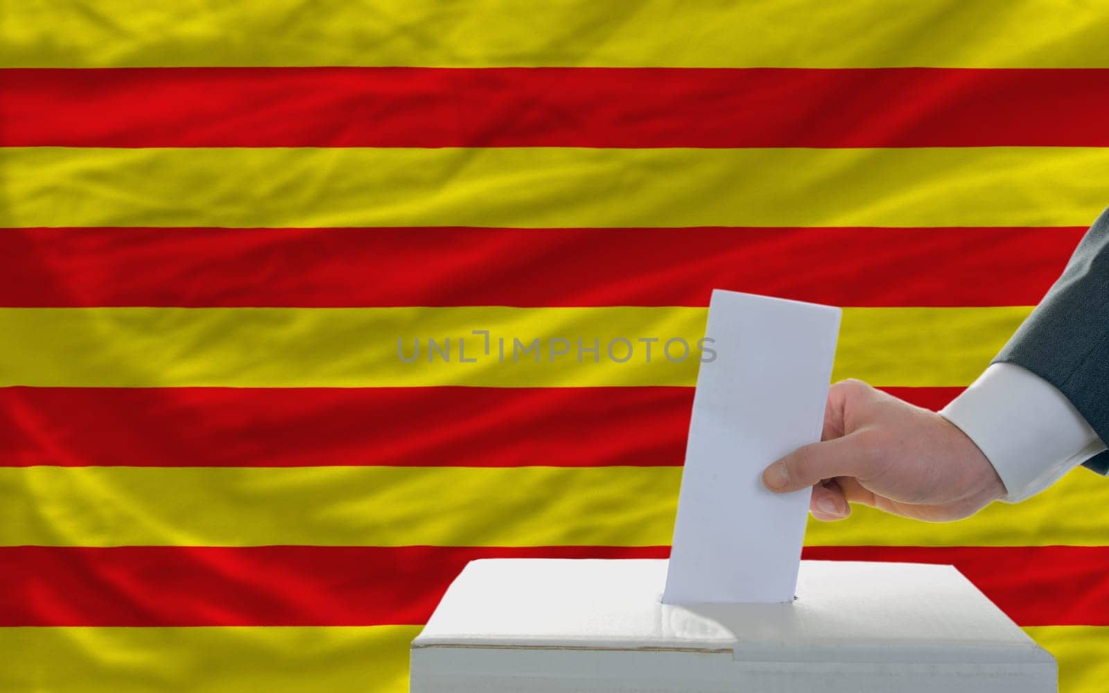 man putting ballot in a box during elections  in front of national flag of catalonia