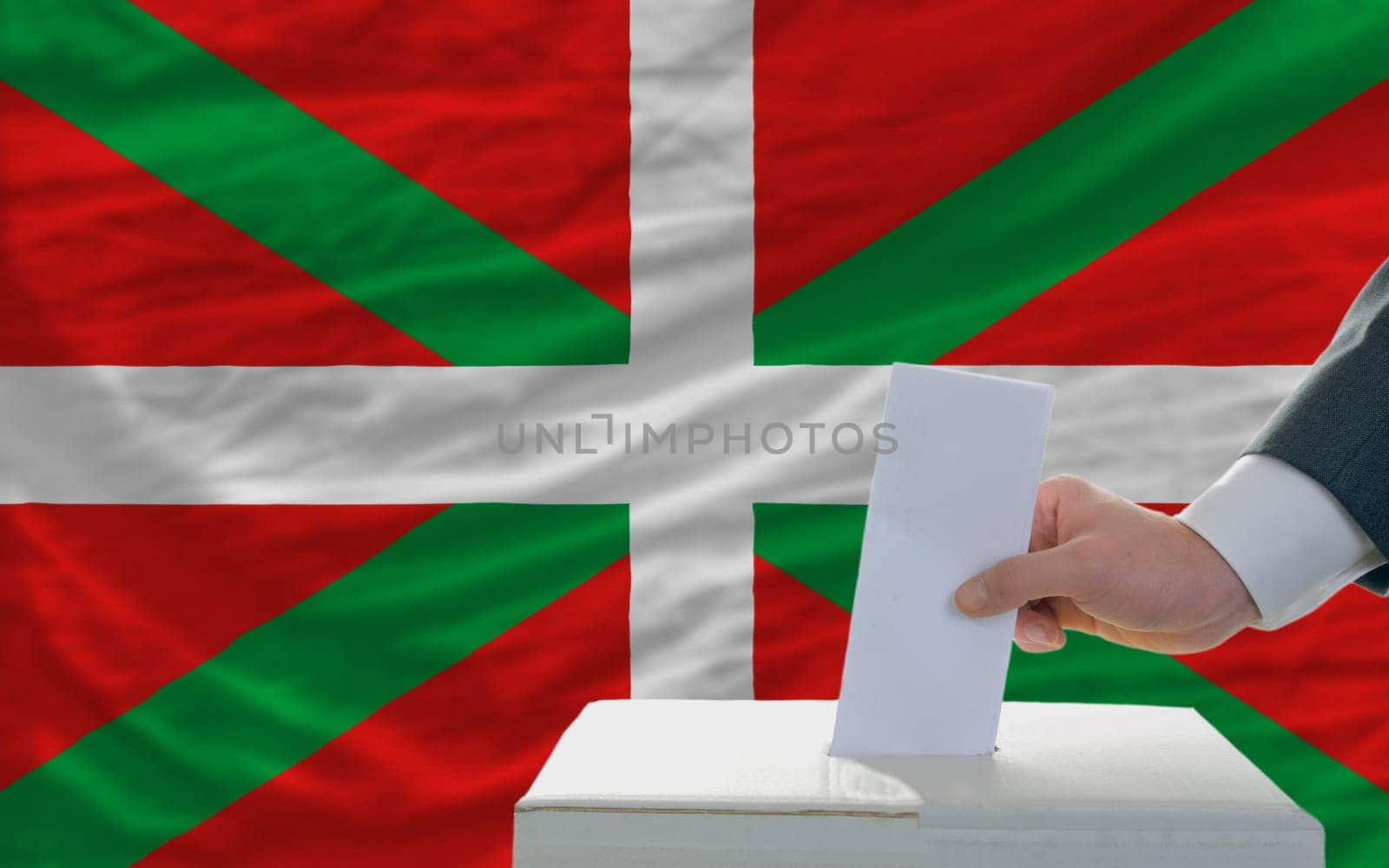 man putting ballot in a box during elections  in front of national flag of basque