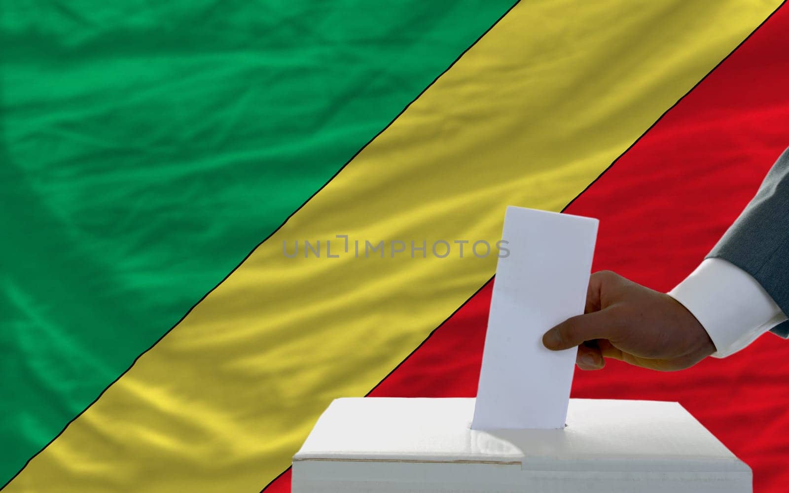 man putting ballot in a box during elections  in front of national flag of congo