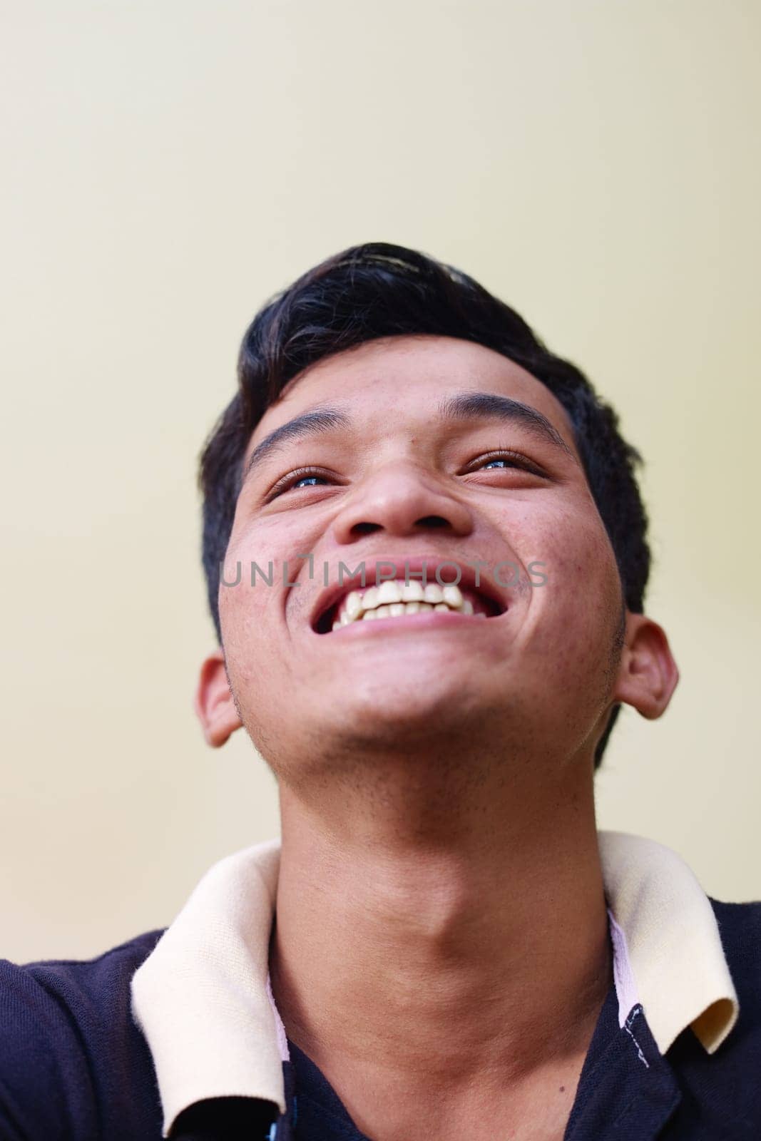 Portrait of happy young asian man smiling and looking up against yellow wall. Copy space