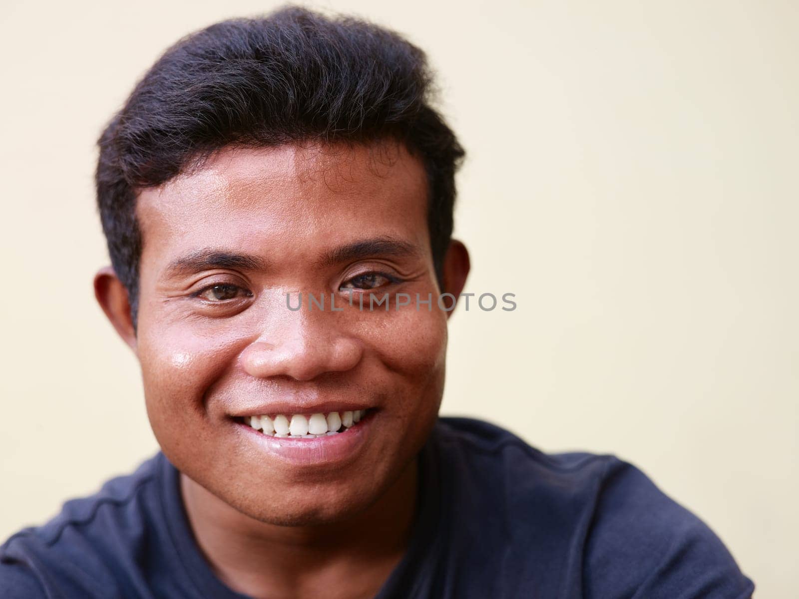 Portrait of happy young asian man smiling and looking at camera against yellow wall. Copy space