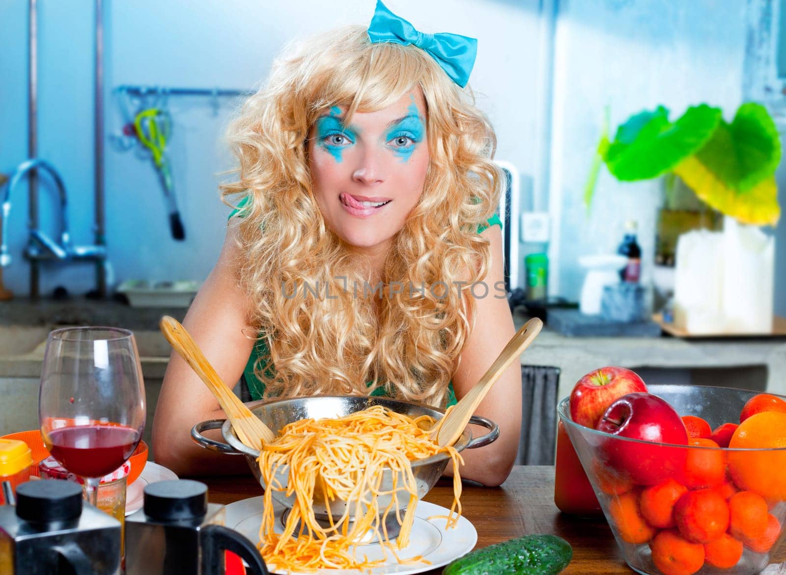 Blonde hungry girl funny on kitchen with pasta and fashion blue makeup