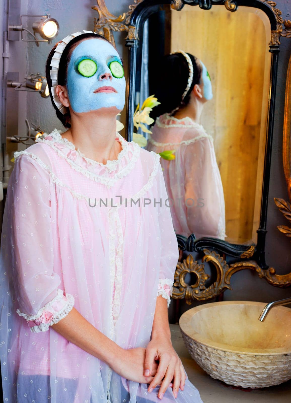 Funny housewife beauty green clay mask and cucumber at the mirror