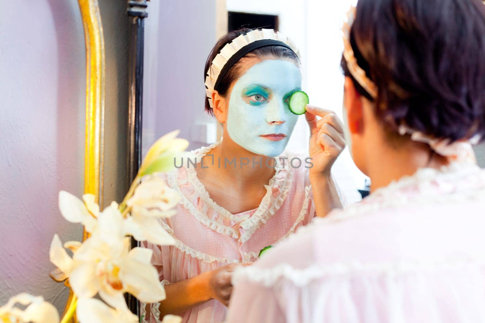 Funny housewife beauty green clay mask and cucumber at the mirror