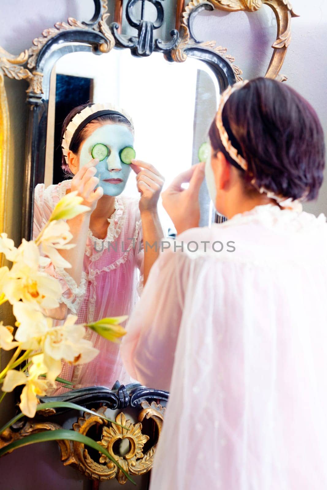 Funny housewife beauty green clay mask and cucumber at the mirror