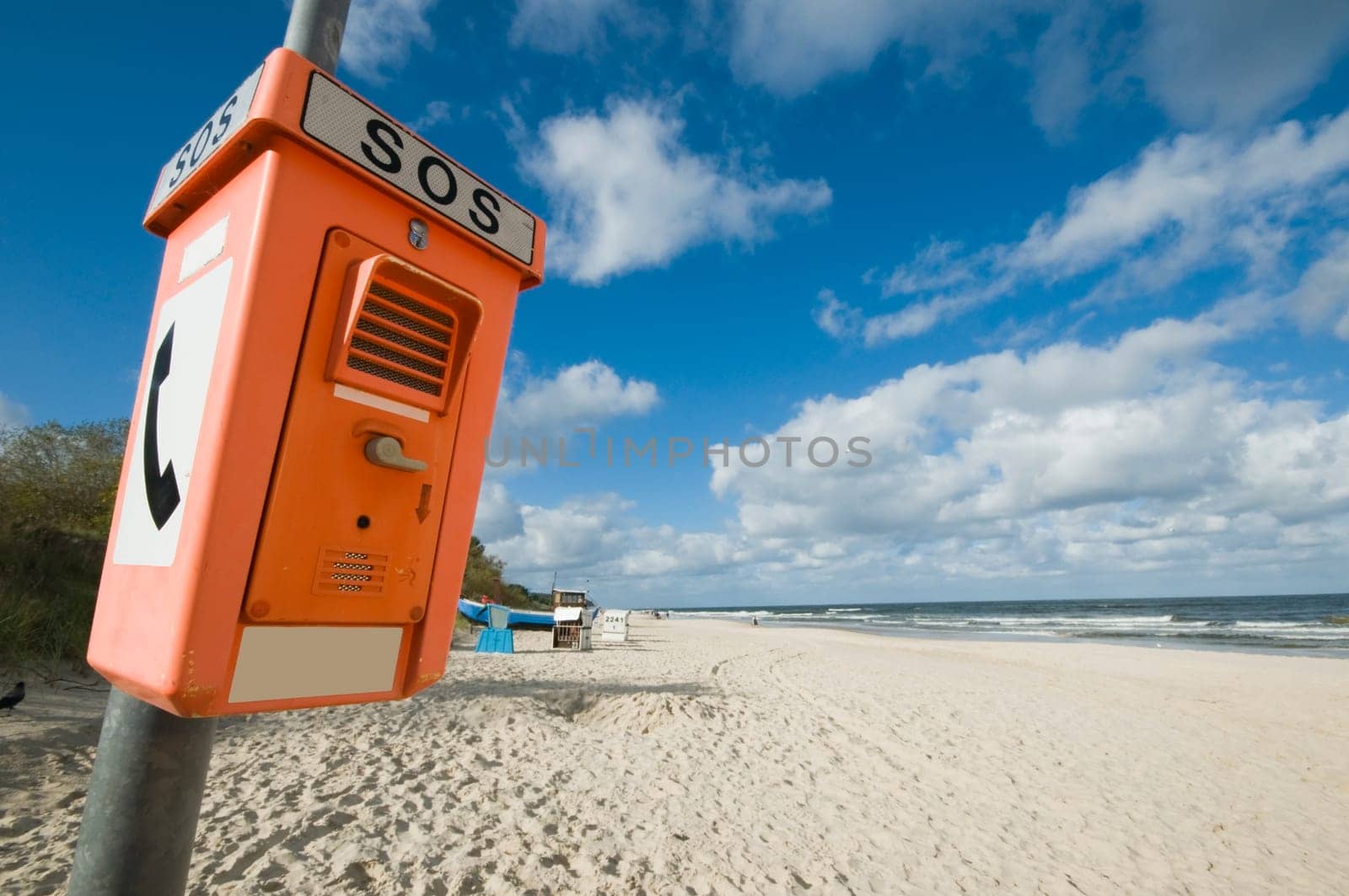 Orange emergency call box on the Baltic Sea beach in summer with blue sky with isolated fair-weather clouds in wide-angle perspective