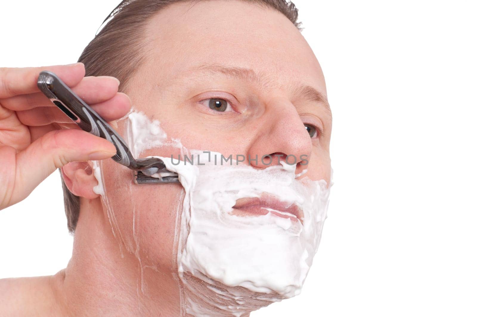 A man with shaving cream on his face shaving wet with a razor