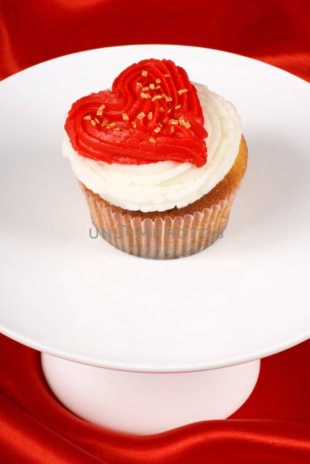 Fancy Valentine&#039 s day cupcake frosted with a red heart shape on a white tray over a red background. With copyspace.