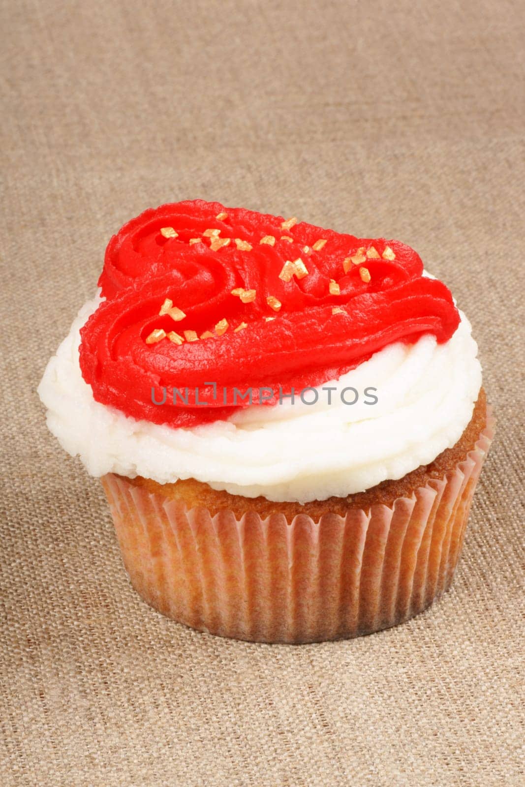 Fancy Valentine&#039 s day cupcake frosted with a red heart shape over a natural jute background. With copy-space