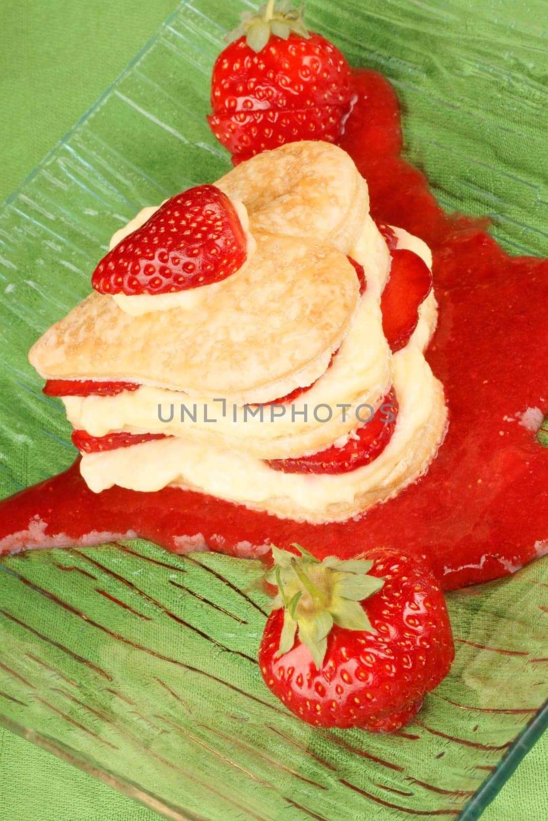 Heart shaped strawberries and custard millefeuille on a strawberry sauce, over a green background. For a sweet Valentine&#039 s Day. Selective focus.