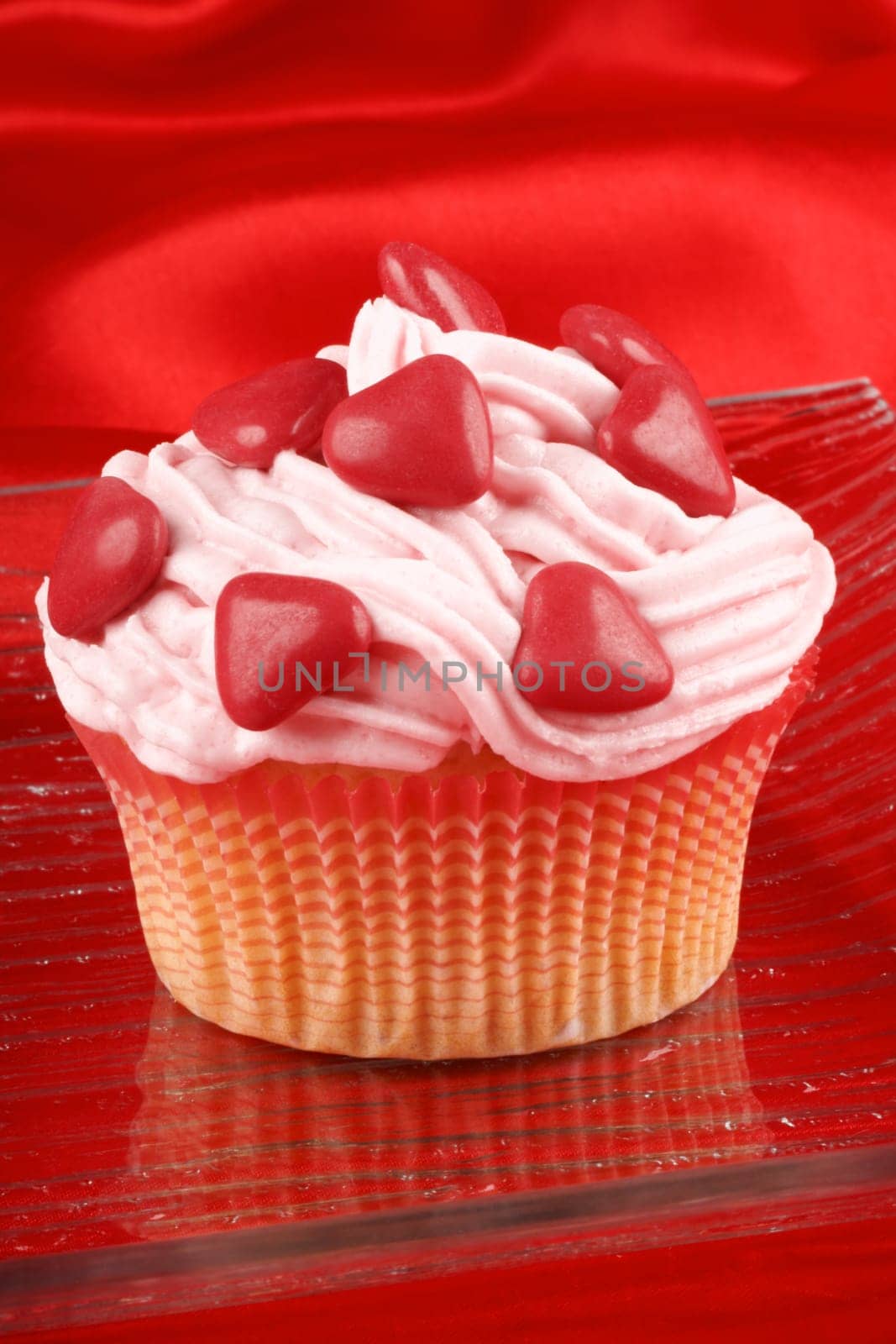 Fancy Valentine&#039 s Day cupcake decorated with small red sugar-coated hearts, over a red background. Selective focus.