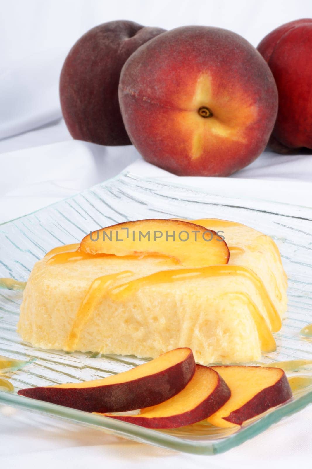 Heart shaped peach bavarian cream dessert with peach sauce and peach slices on a transparent glass plate over a white background.