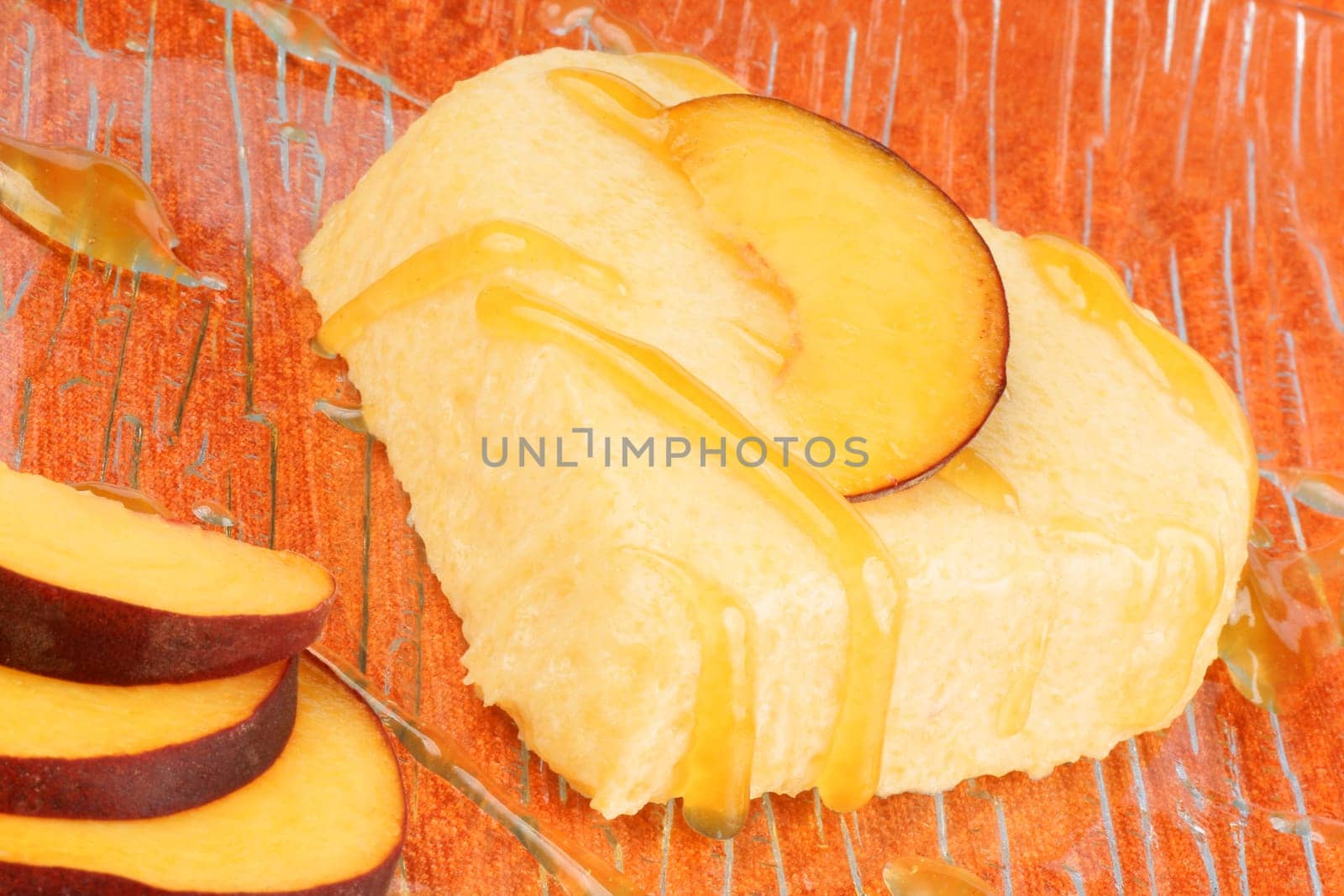 Heart shaped peach bavarian cream dessert with peach sauce and peach slices on a transparent glass plate over an orange background.