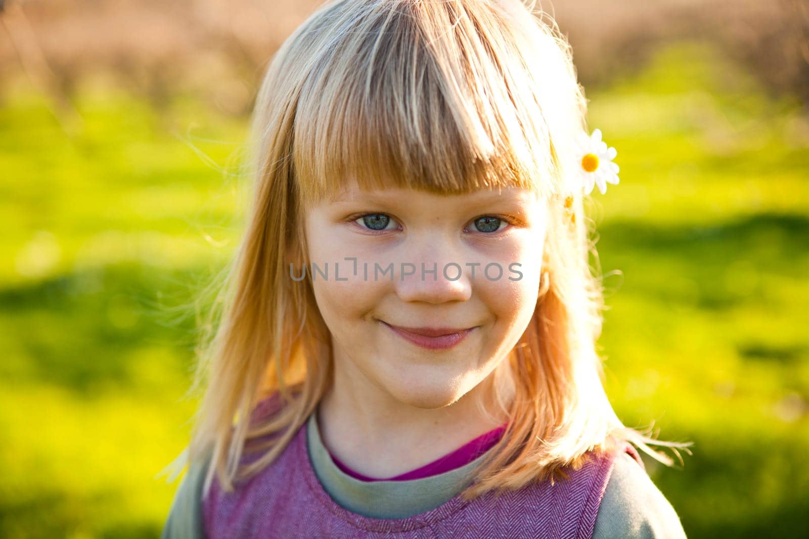 Cute little girl outdoors on a green field with flower in her hair