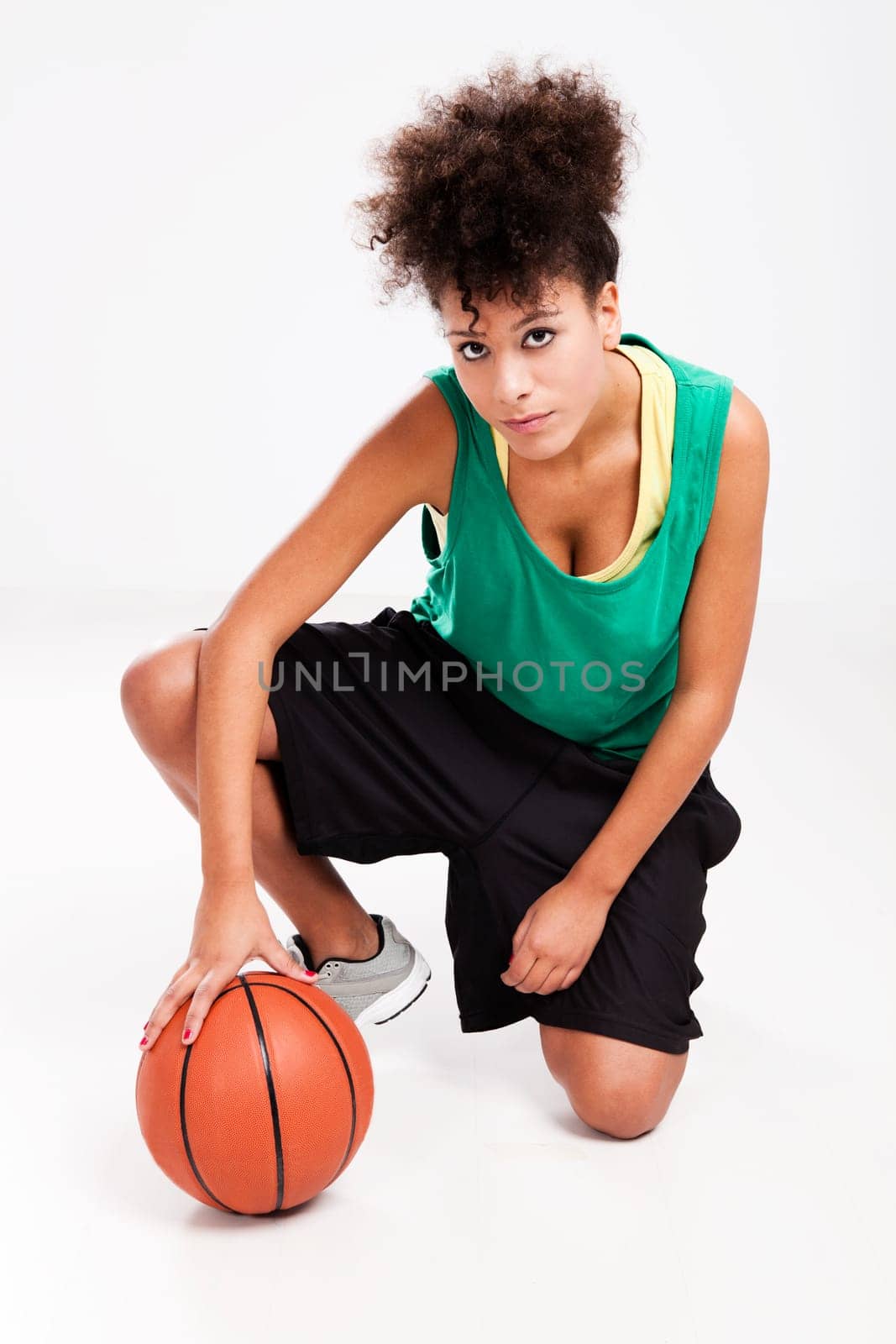 Athletic woman kneeling with a basketball. Studio shot.