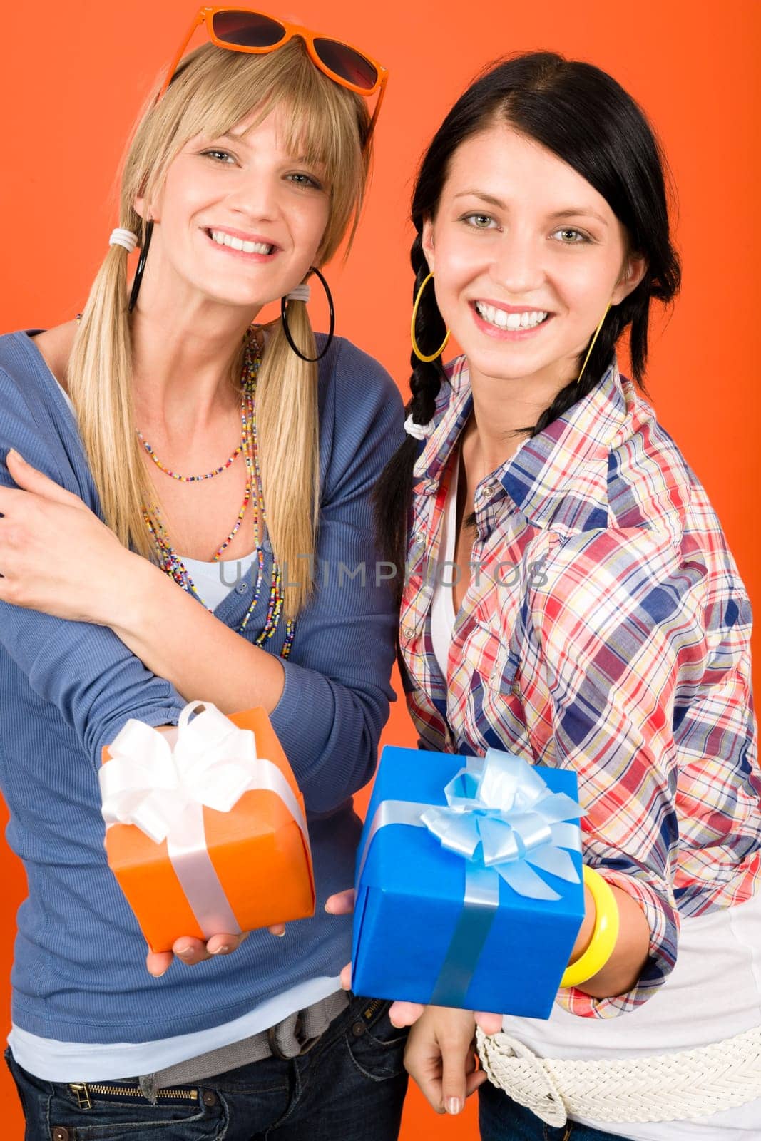 Two young woman friends hold party presents smiling orange background