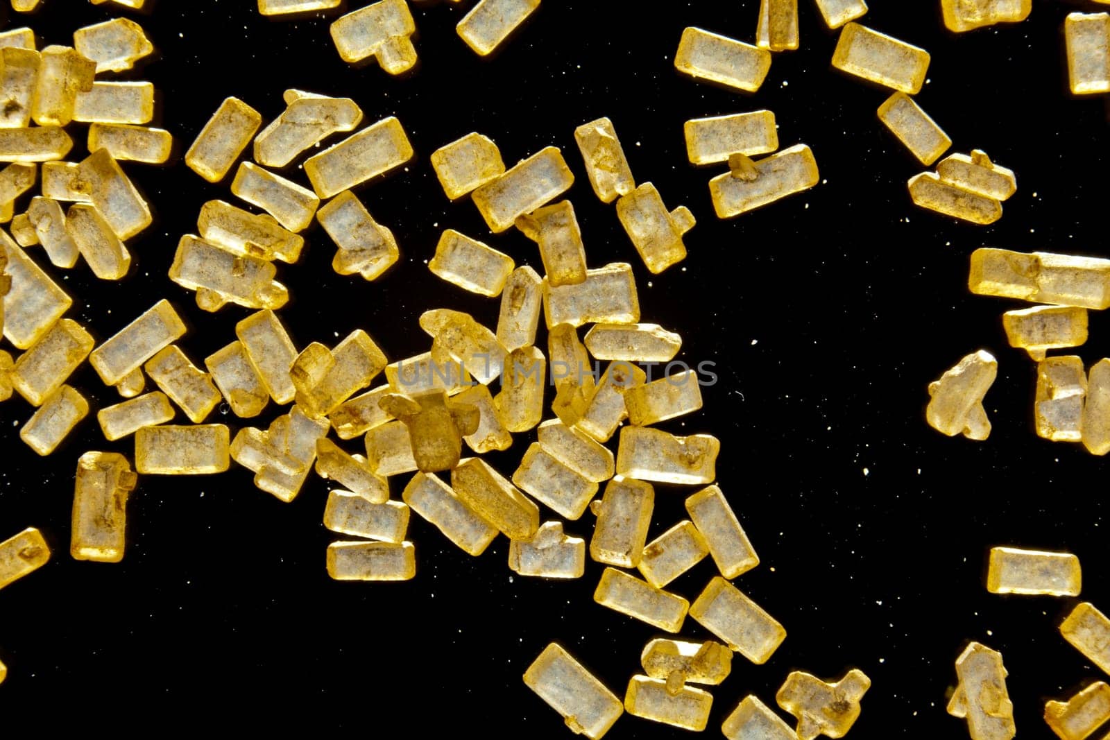 Macro of refined crystallised sugar with rectangular golden granules on a dark background