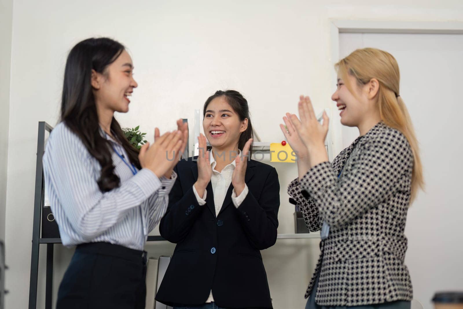 A diverse group of businesswomen applauds each other in an office, showcasing teamwork and celebrating their achievements.