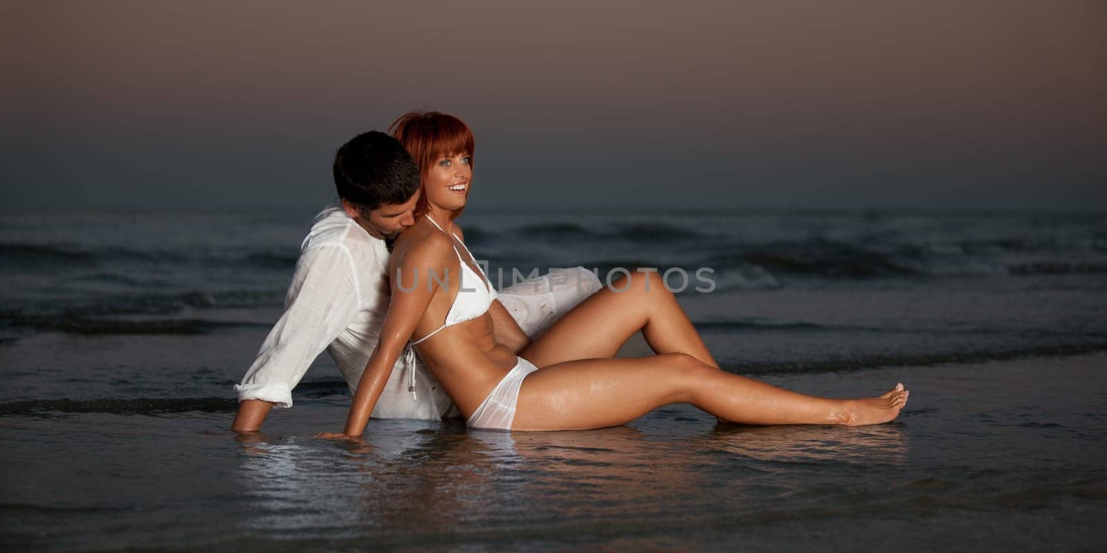 happy, young couple, dressed in white, kissing, hugging on a desert beach shore, at sunset