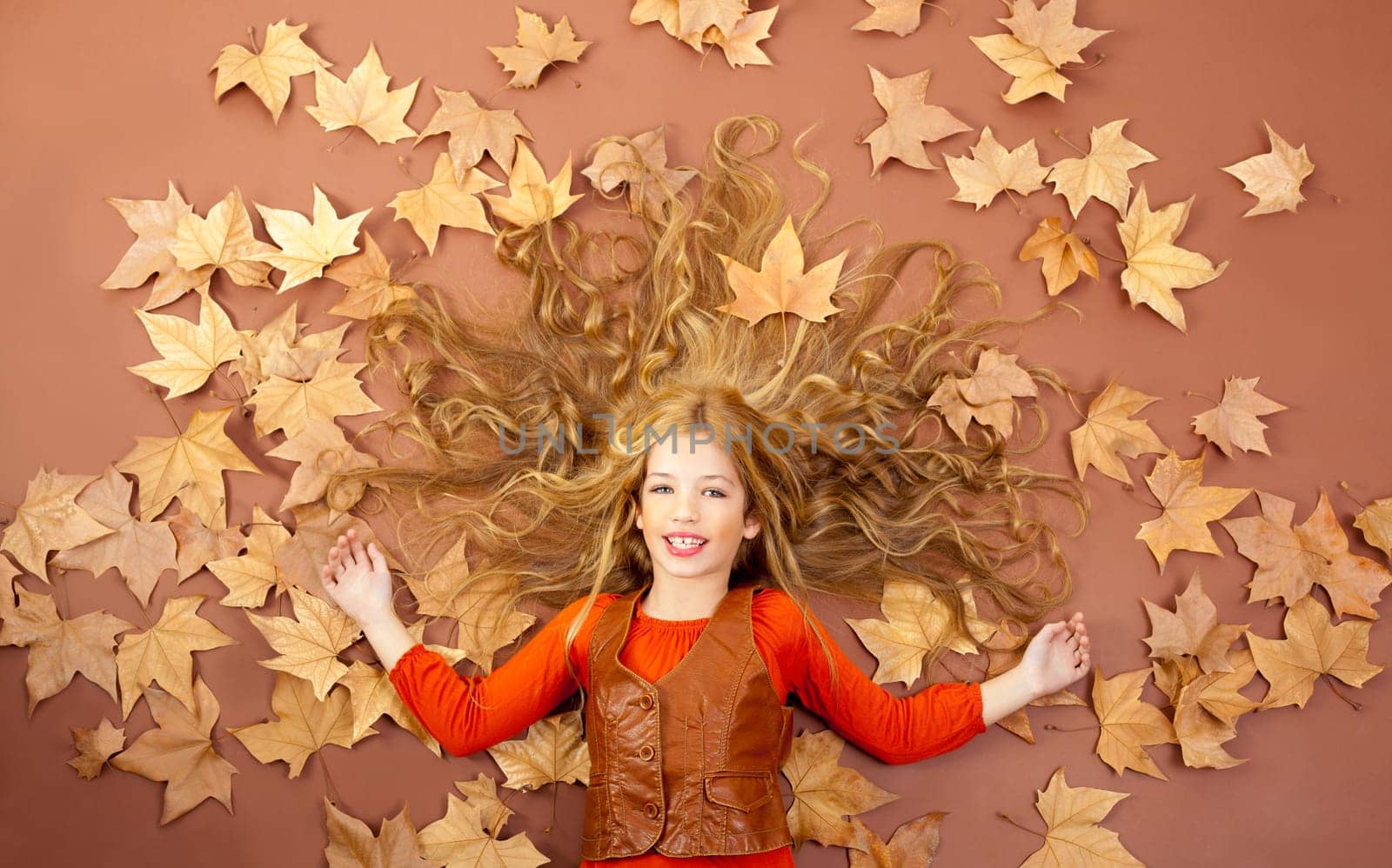 autumn fall little blond girl on dried tree leaves background and long spread hair
