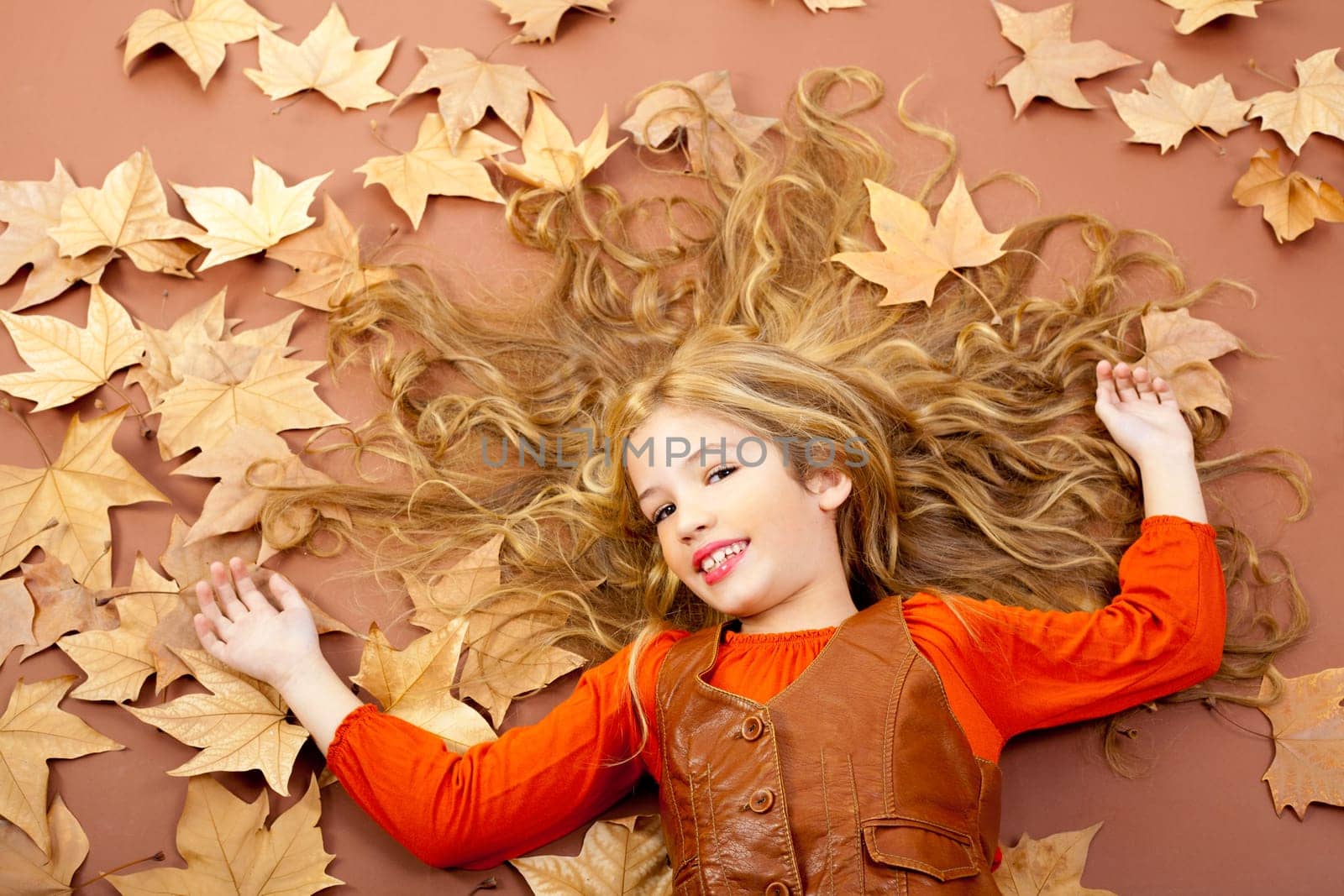 autumn fall little blond girl on dried tree leaves background and long spread hair