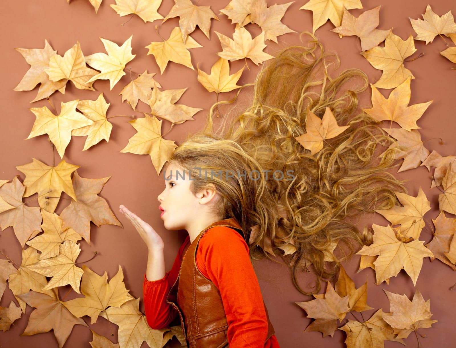 autumn fall little blond girl on dried tree leaves blowing wind with lips